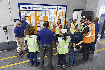 Leadec employees standing in front of a display board discussing tasks.