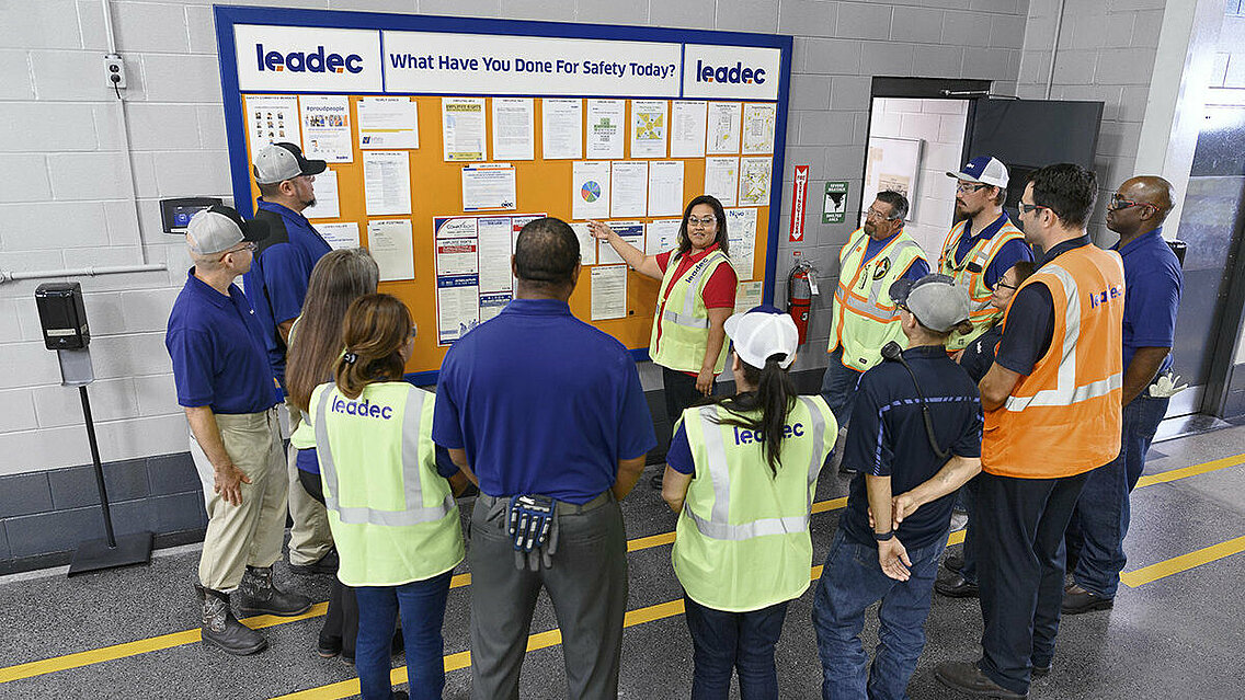 Leadec employees standing in front of a display board discussing tasks.