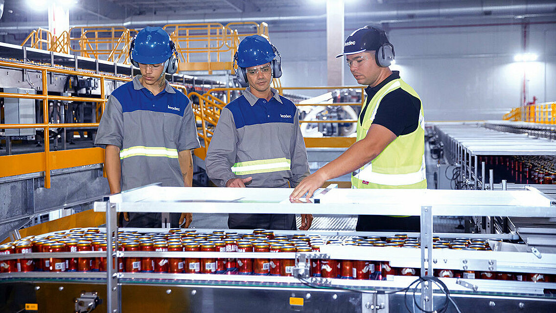 Three Leadec employees inspecting conveyor belt for drinks in a beverage factory. 