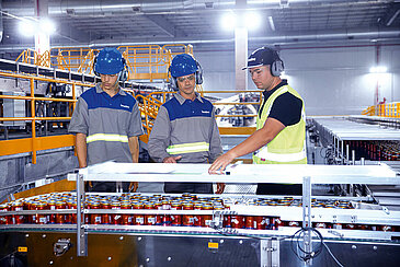 Three Leadec employees inspecting conveyor belt for drinks in a beverage factory. 