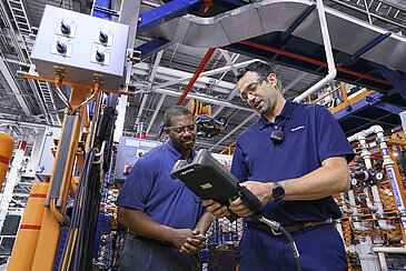 Two Leadec employees working with a controller at a robot to optimize processes.